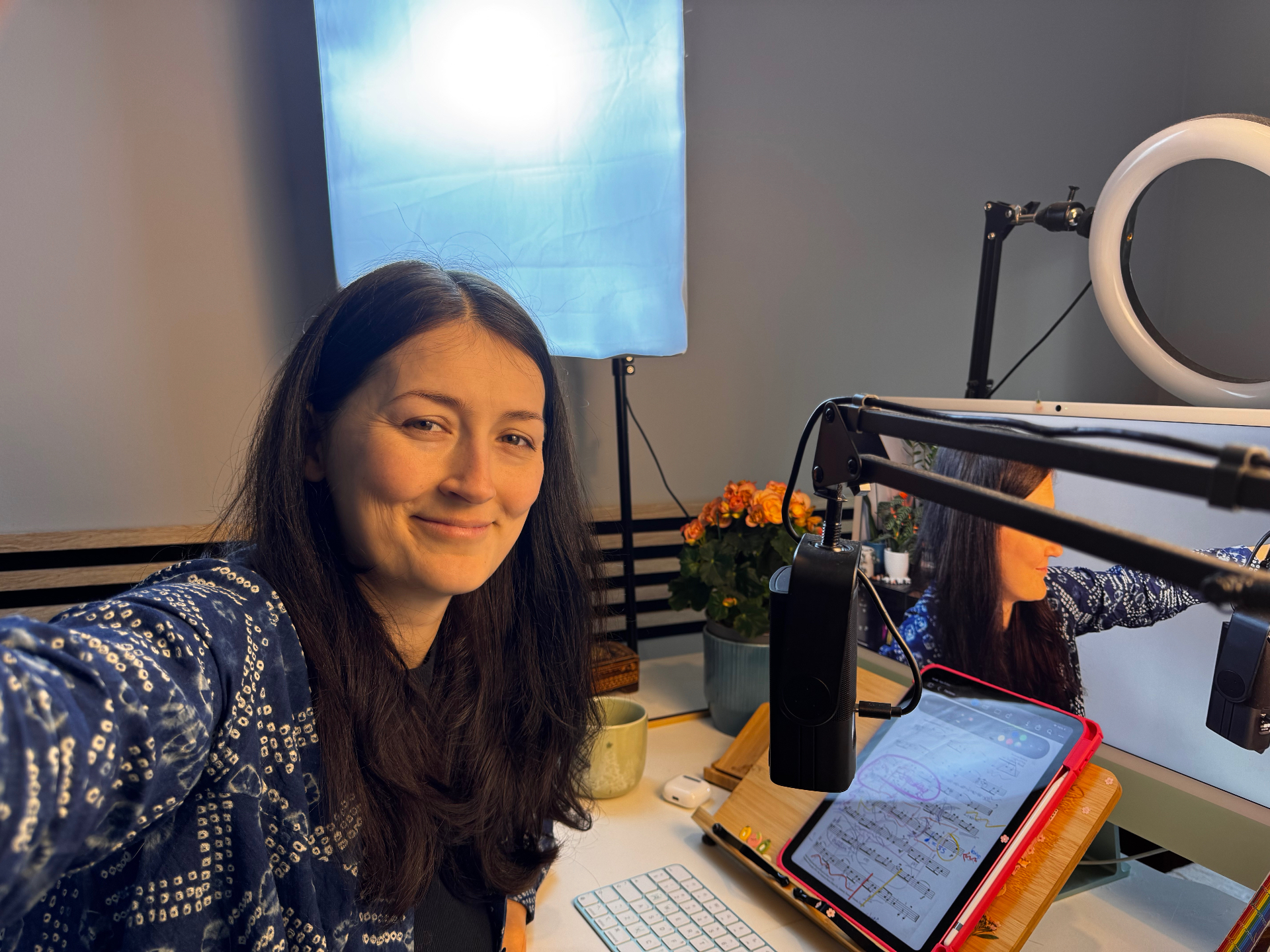 Ilona smiling at her home teaching desk with a softbox light, ring light, microphone, and tablet showing sheet music